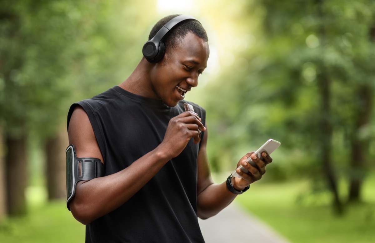 male runner eating protein bar while outside wearing headphones