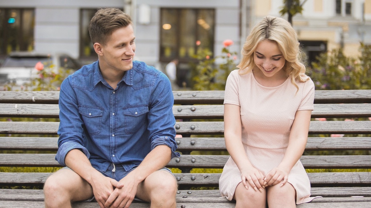 Man sitting next to giggling woman on park bench