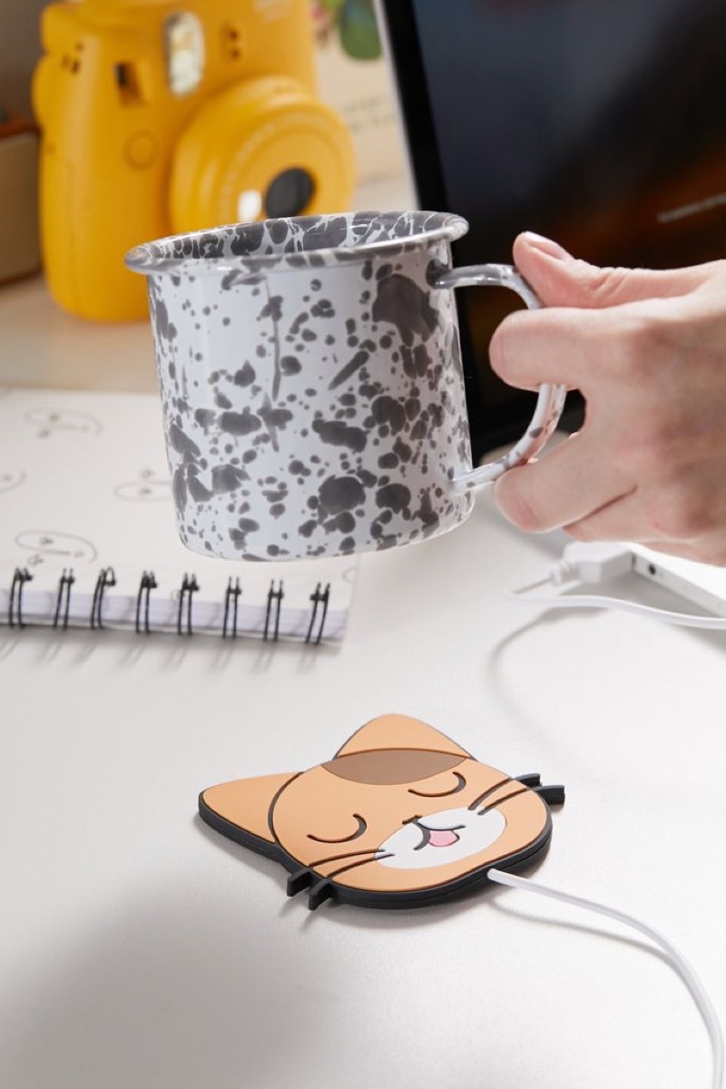 white hand holding speckled cup over cat heater