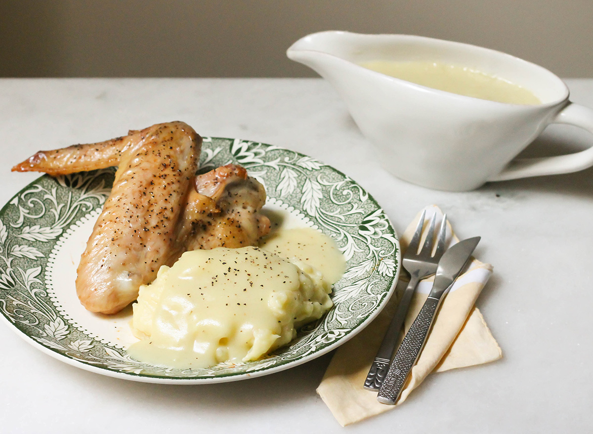 Homemade gravy in a boat with turkey wing and mashed potatoes seasoned