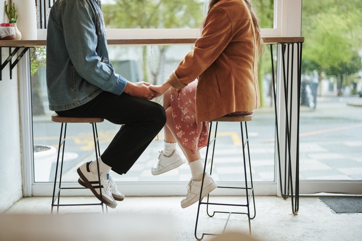 Unrecognizable young couple holding hands while sitting together by a window in a cafe during a date