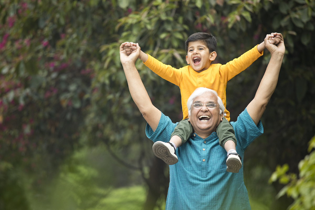 Carefree grandfather carrying grandson on shoulders at park