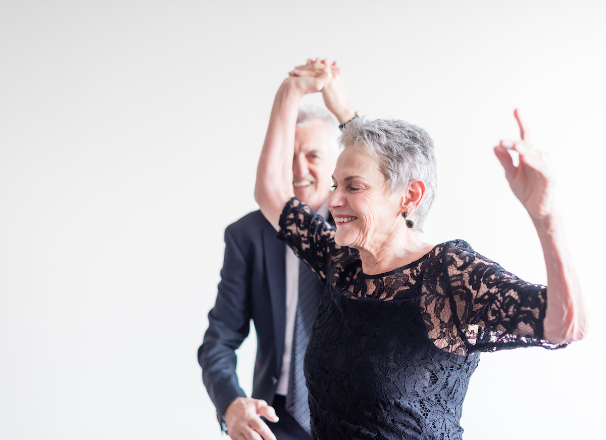 Close up of elegantly dressed older man and woman dancing exuberantly against neutral background