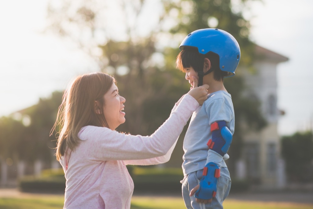 Mom helping her son put on a helmet.