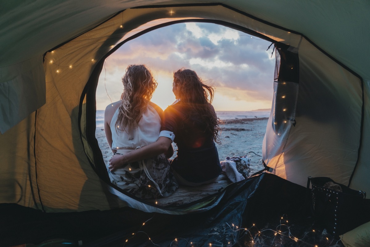 Young adult lesbian couple admiring the sunset in a tent on the beach on vacation