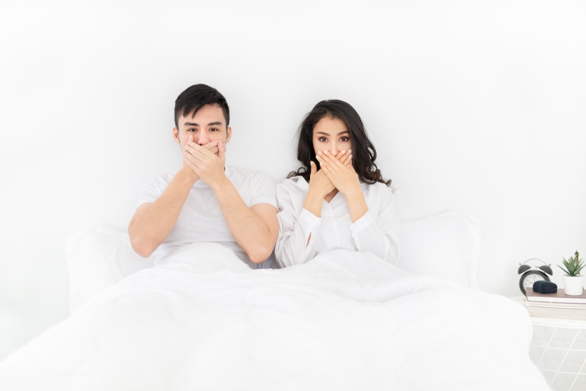 Couple Covering Their Mouths While In Bed