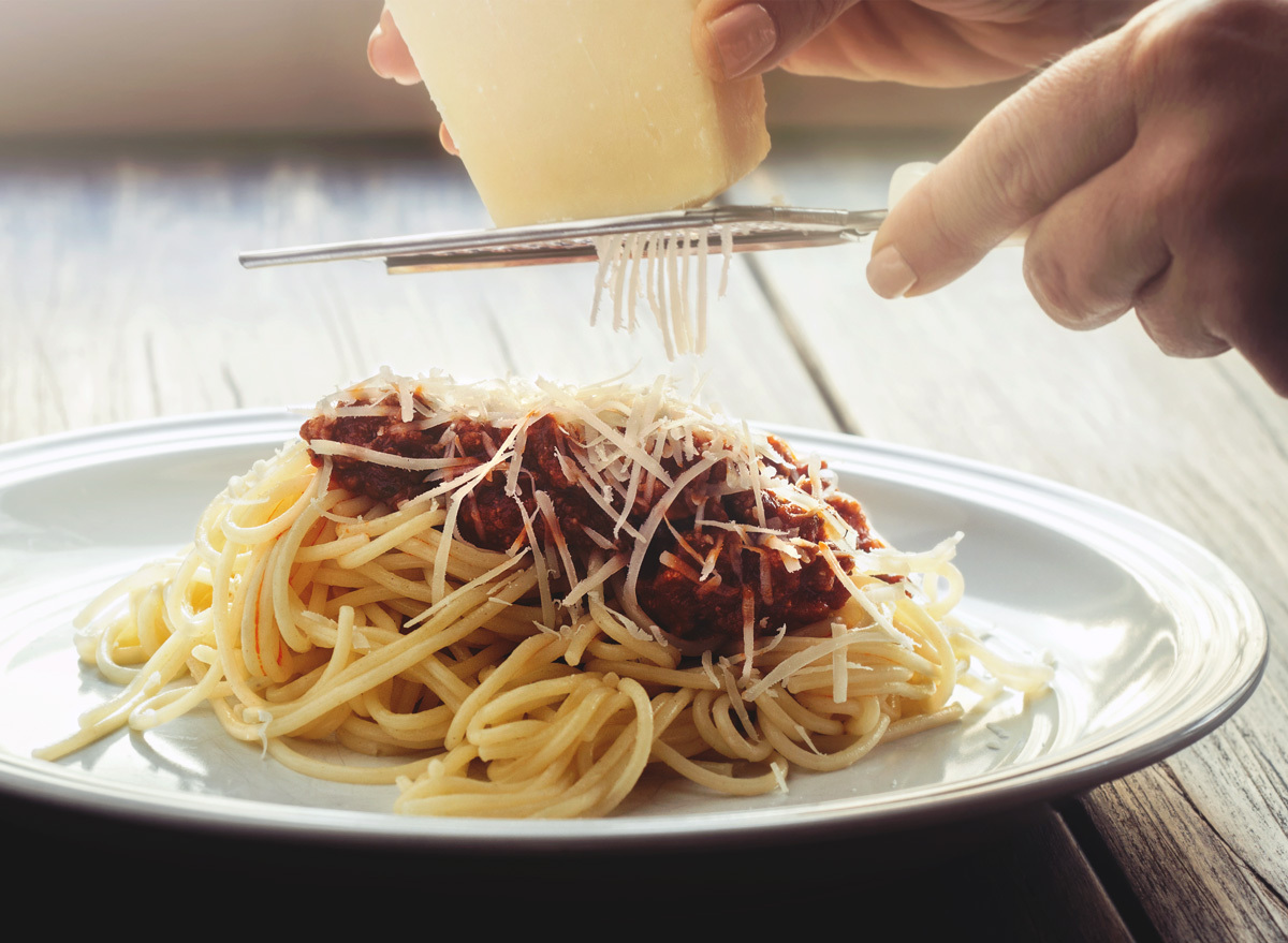 Grating parmesan cheese on pasta with red sauce