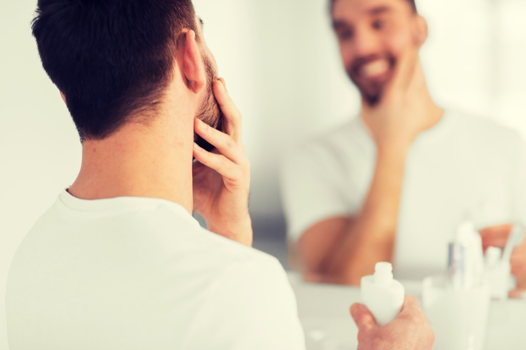 a well-groomed man stroking his beard in the bathroom