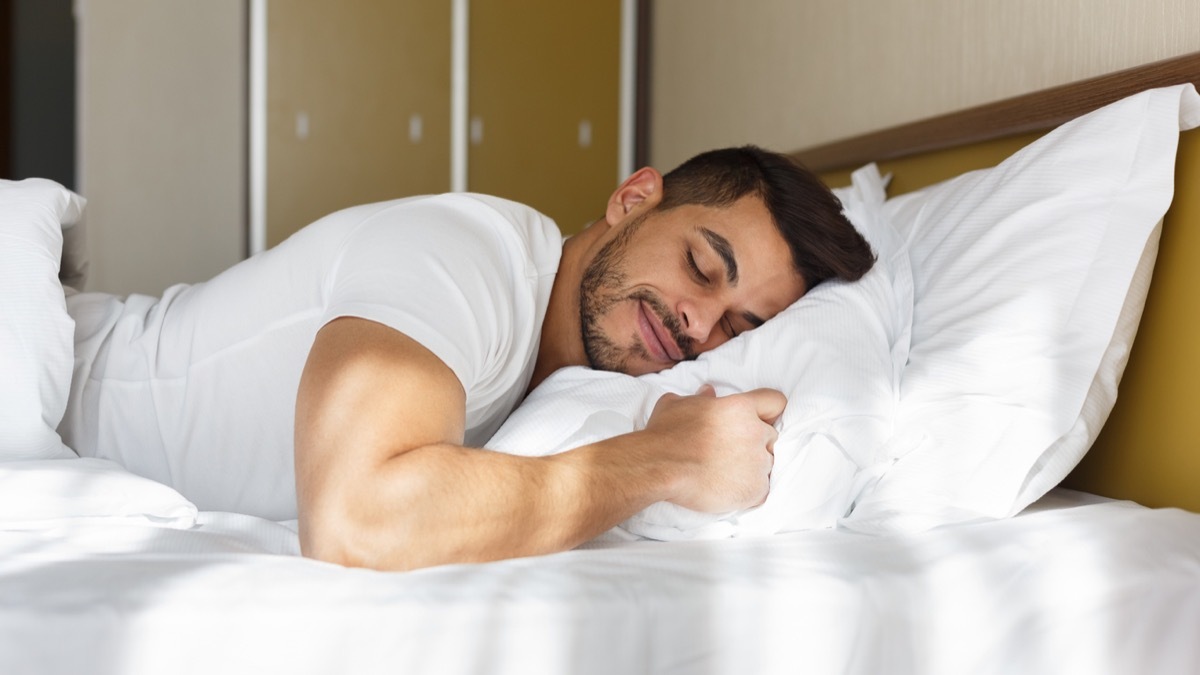 young latino man smiling with his eyes closed while lying on his pillow in bed