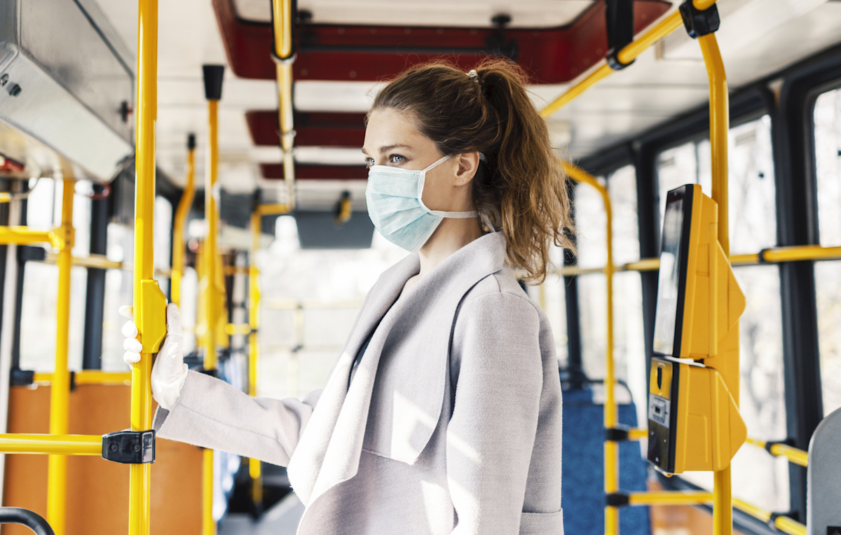 Woman wearing surgical protective mask going to work, holding railing of bus