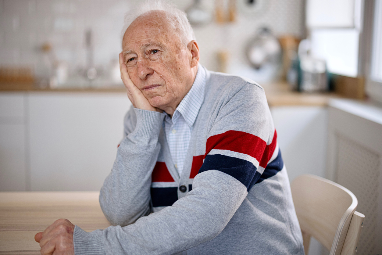 A senior man sitting in his kitchen with a look of apathy