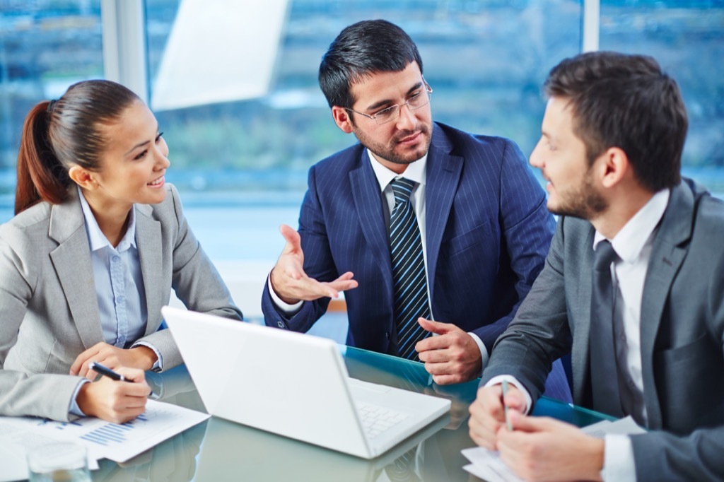 two men and one woman sitting at conference table around a laptop