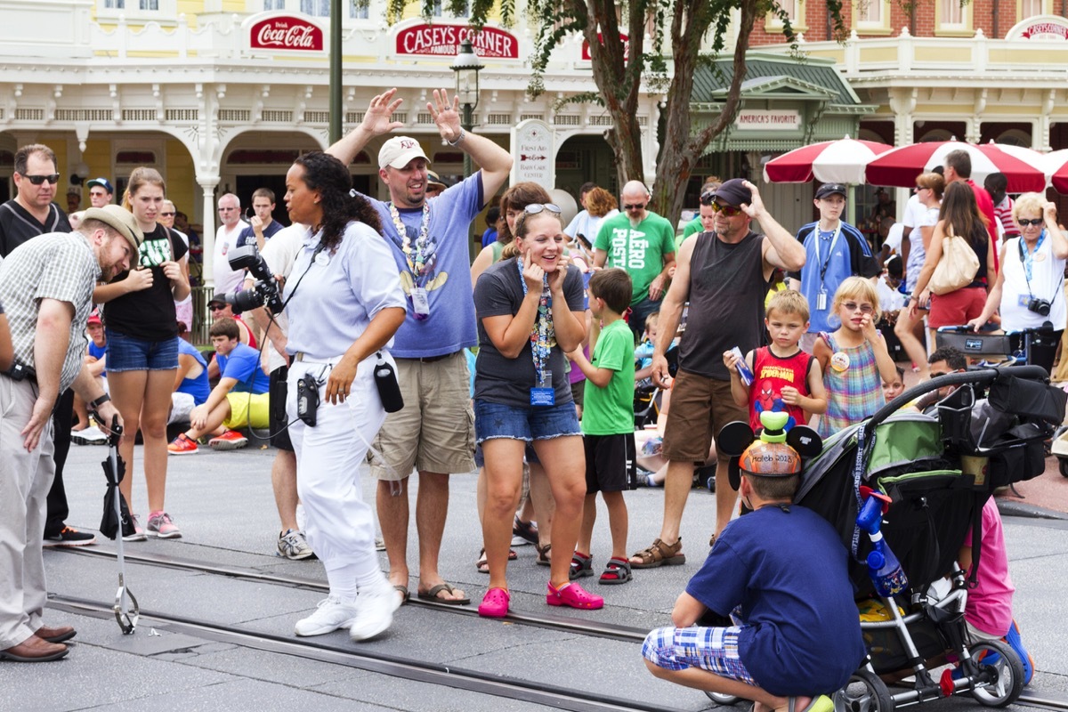 Parents getting their kids attention for a photo at Main Street USA, the entrance to Magic Kingdom amusement park in Walt Disney World. This is a very popular photo spot as the Cinderella's Caste is in the background.