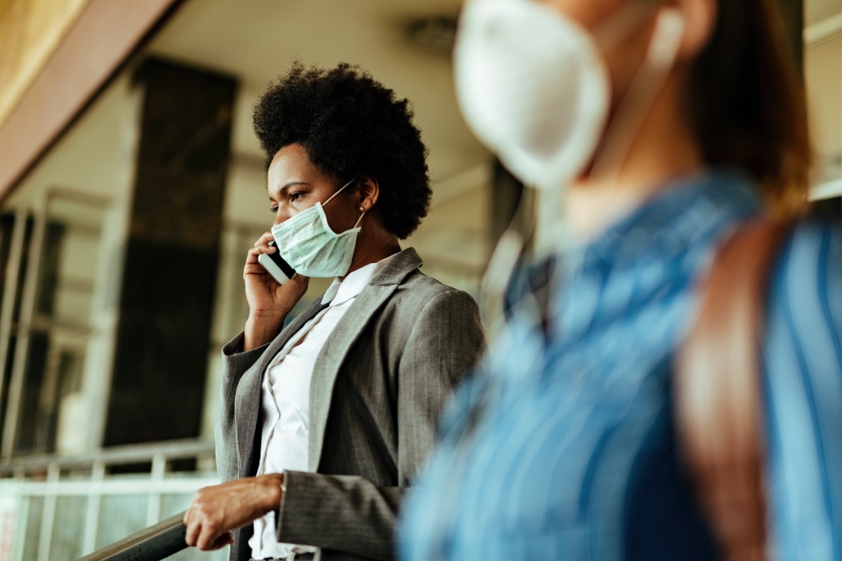 businesswoman wearing face mask as a protection against viruses and talking on mobile phone while walking at airport terminal