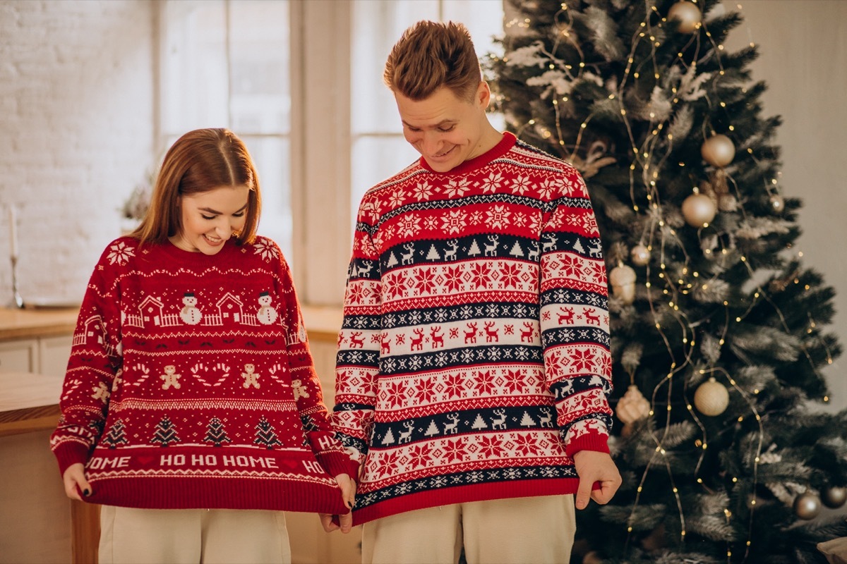 couple wearing Christmas sweaters in front of tree