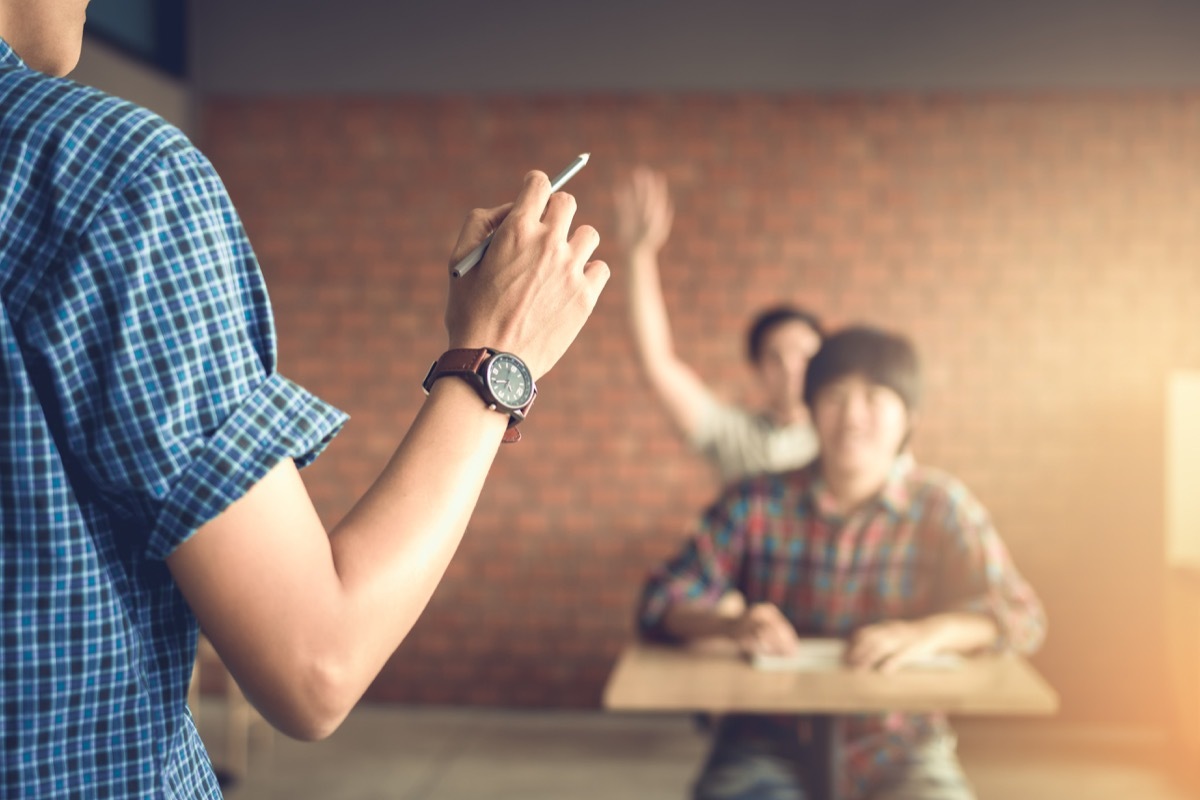 Teacher stands in front of college students, closeup on hand, weird college classes