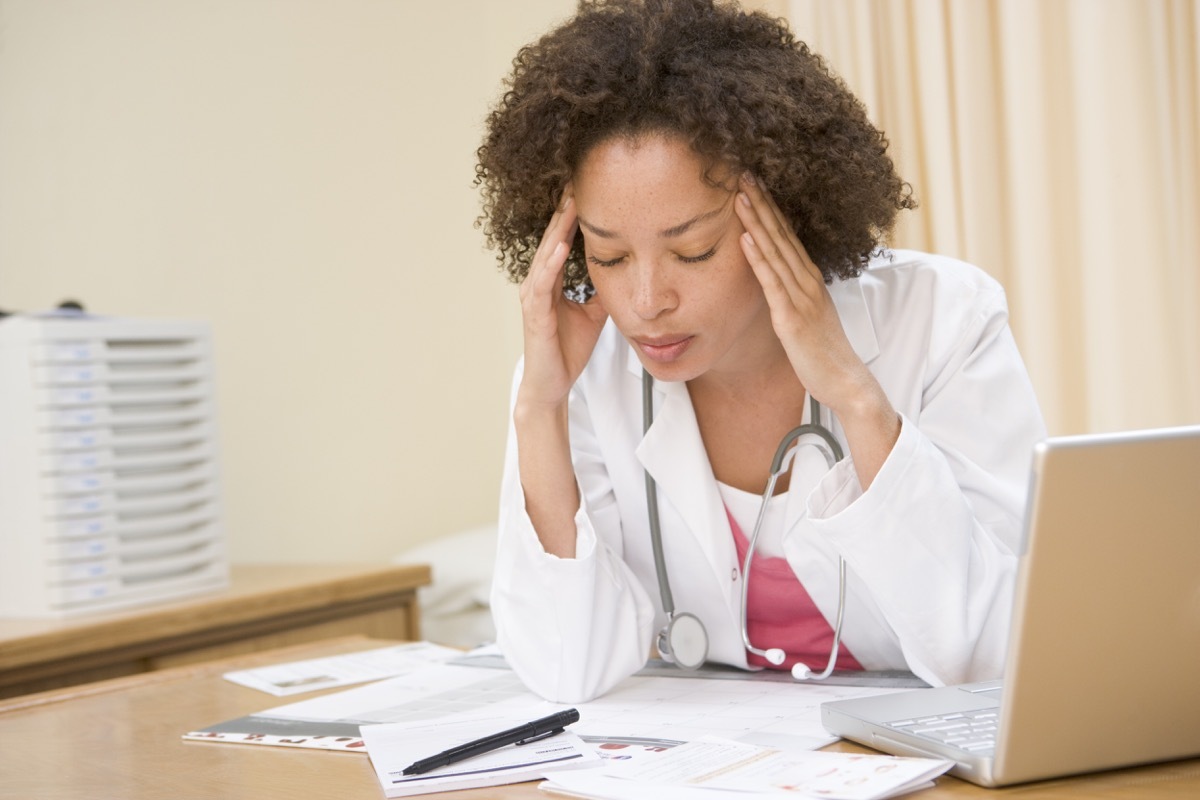 Doctor with laptop and headache in doctor's office