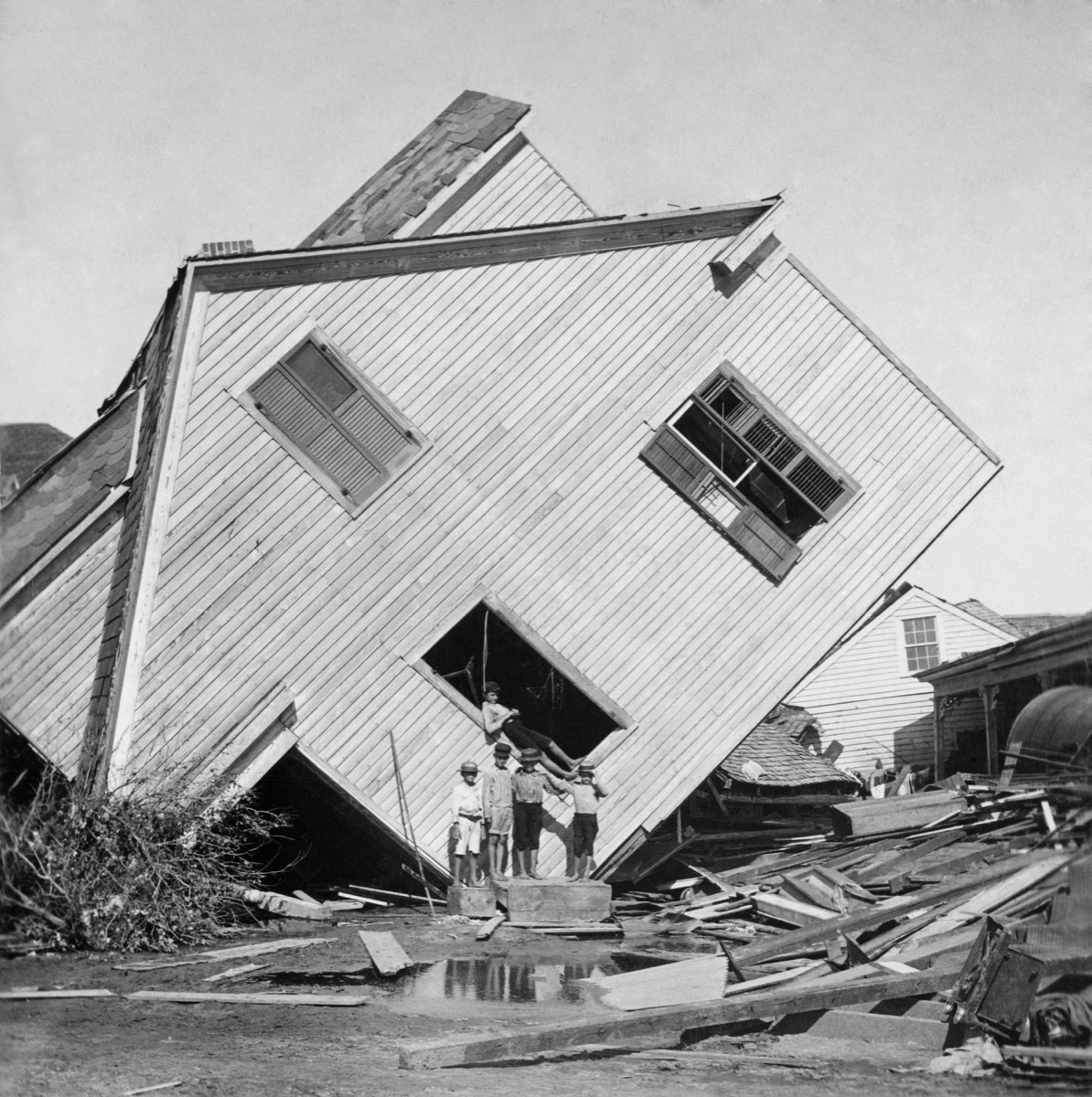 A house tipped on side after the 15 foot storm surge of the Galveston Hurricane of Sept. 1900. Five boys pose in front of the house on Avenue N