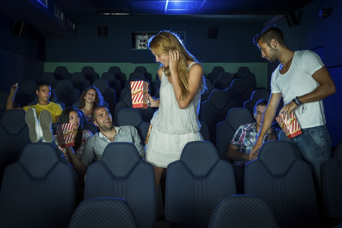 a man and woman holding popcorn squeezing past people sitting down to get to their seats at the movies