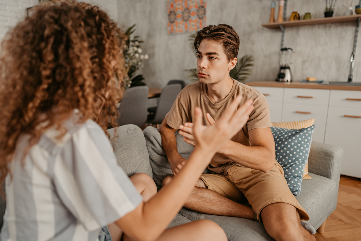 Young couple with relationship problems, sitting on the sofa in the living room and arguing.