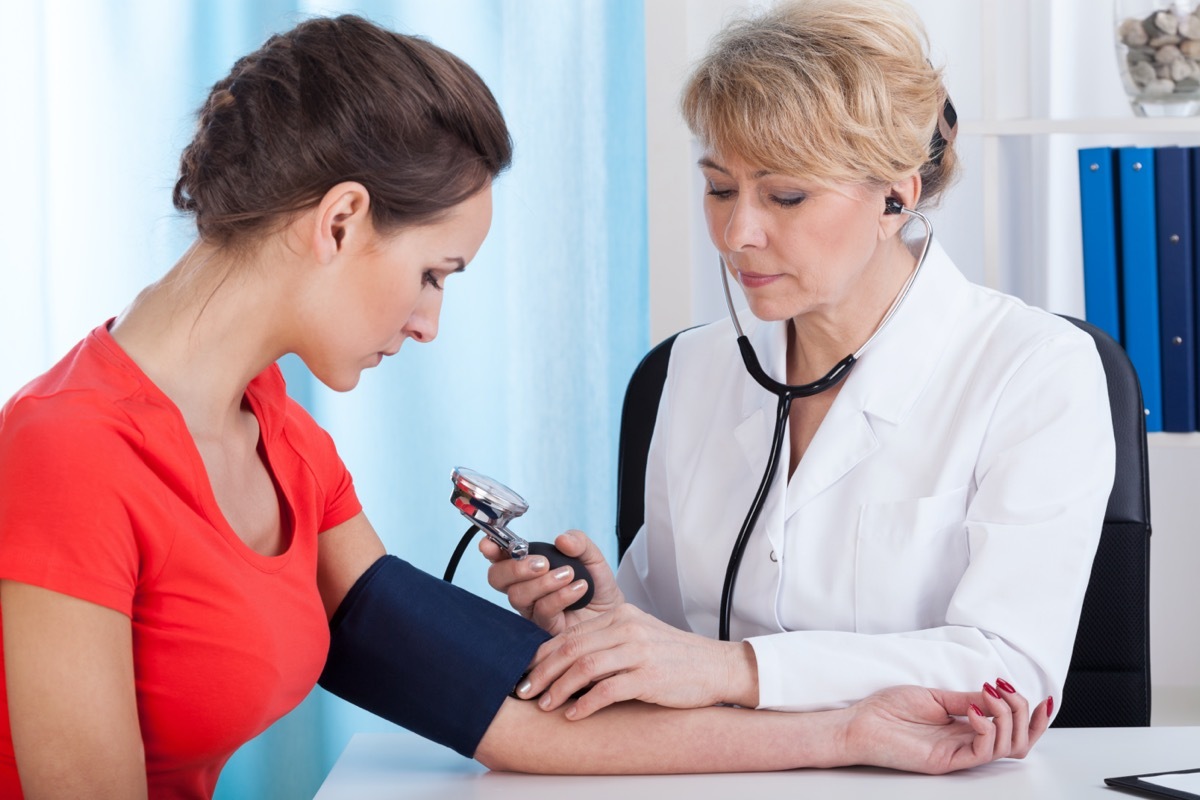 Doctor taking blood pressure of female patient at office