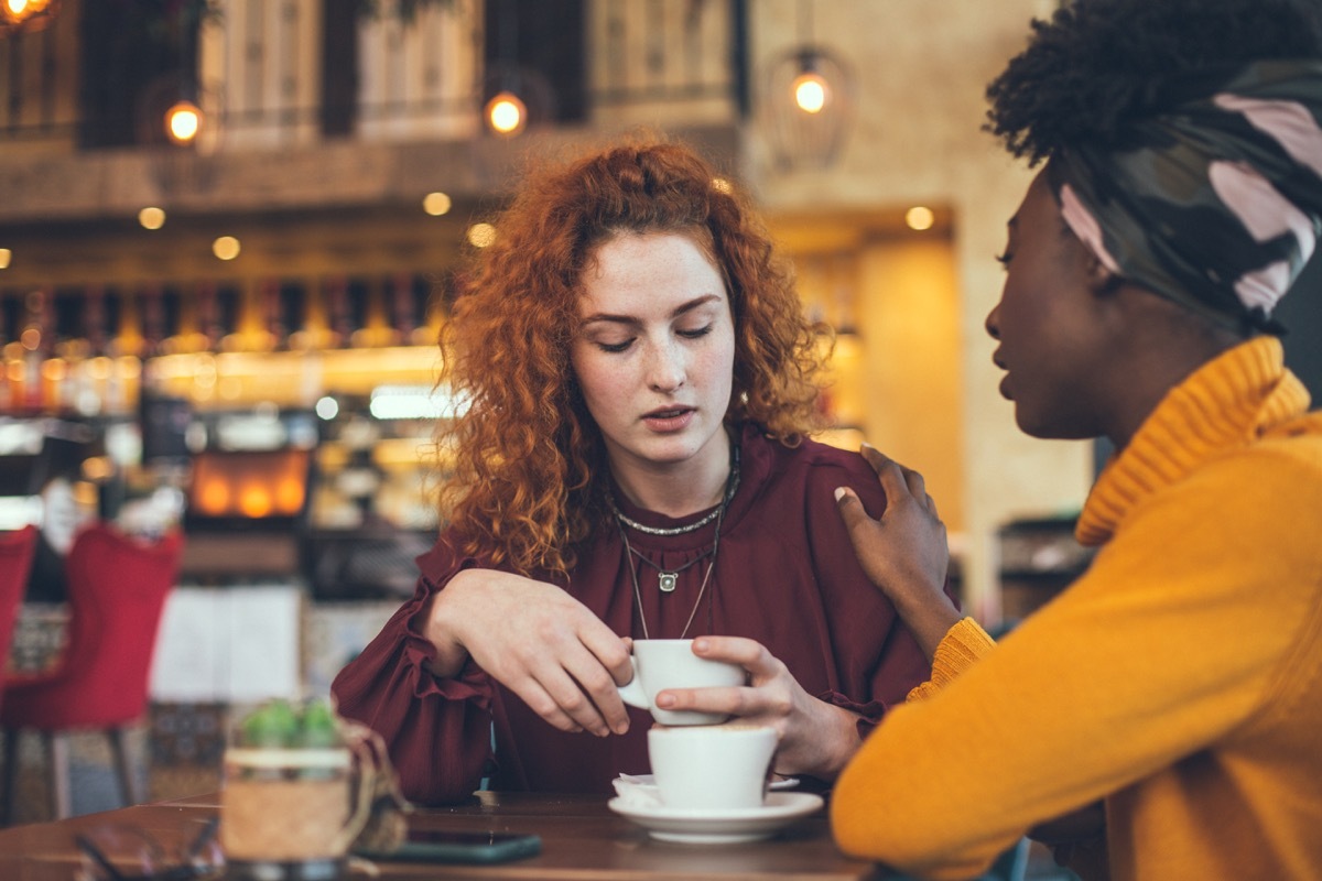 A young woman is talking with a female friend about her problem in a cafe. The friend is supportive and understanding.