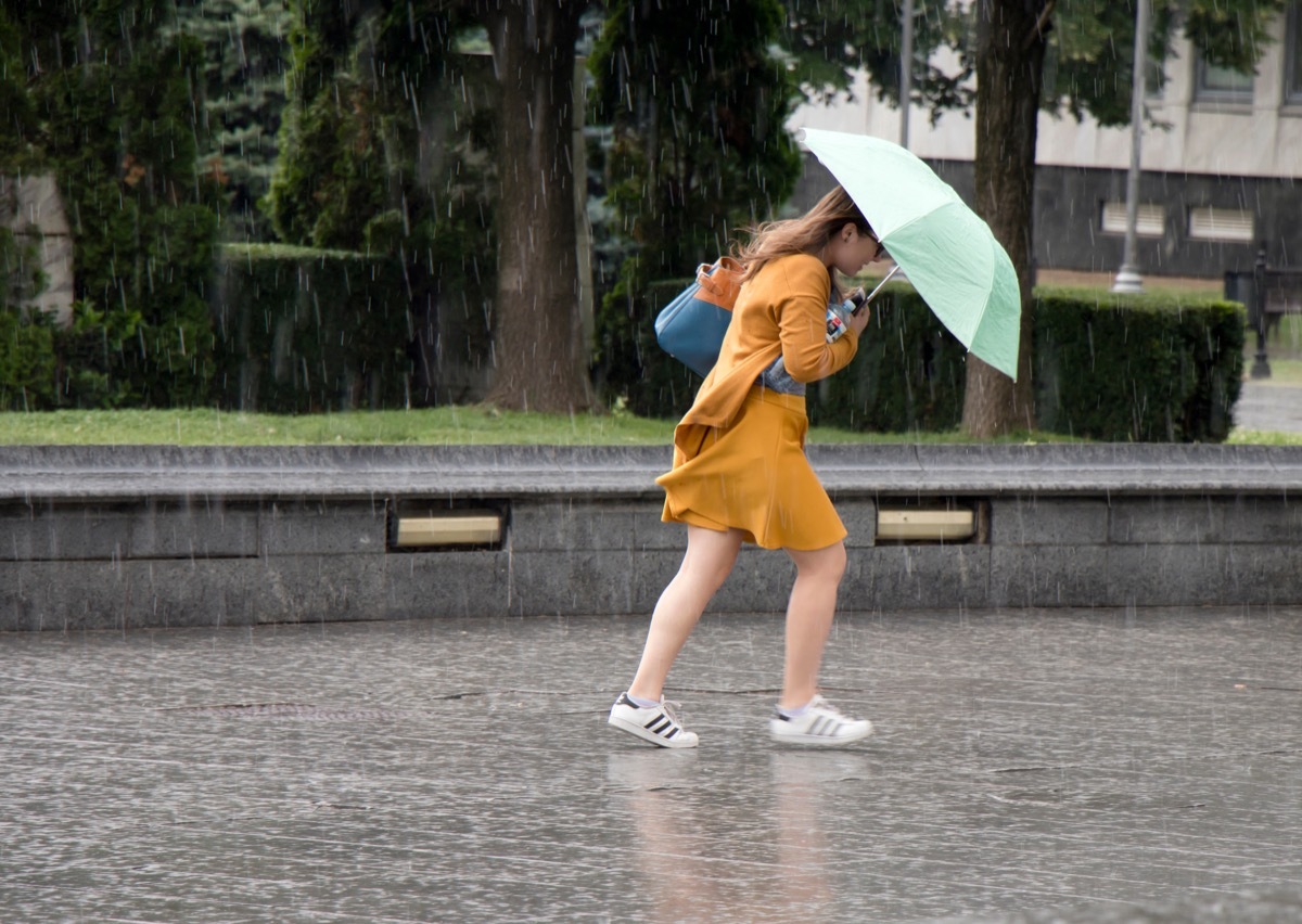 Belgrade, Serbia - June 14, 2018: One young woman running under umbrella in the sudden heavy and windy spring rain in the city park , holding a bottle of water