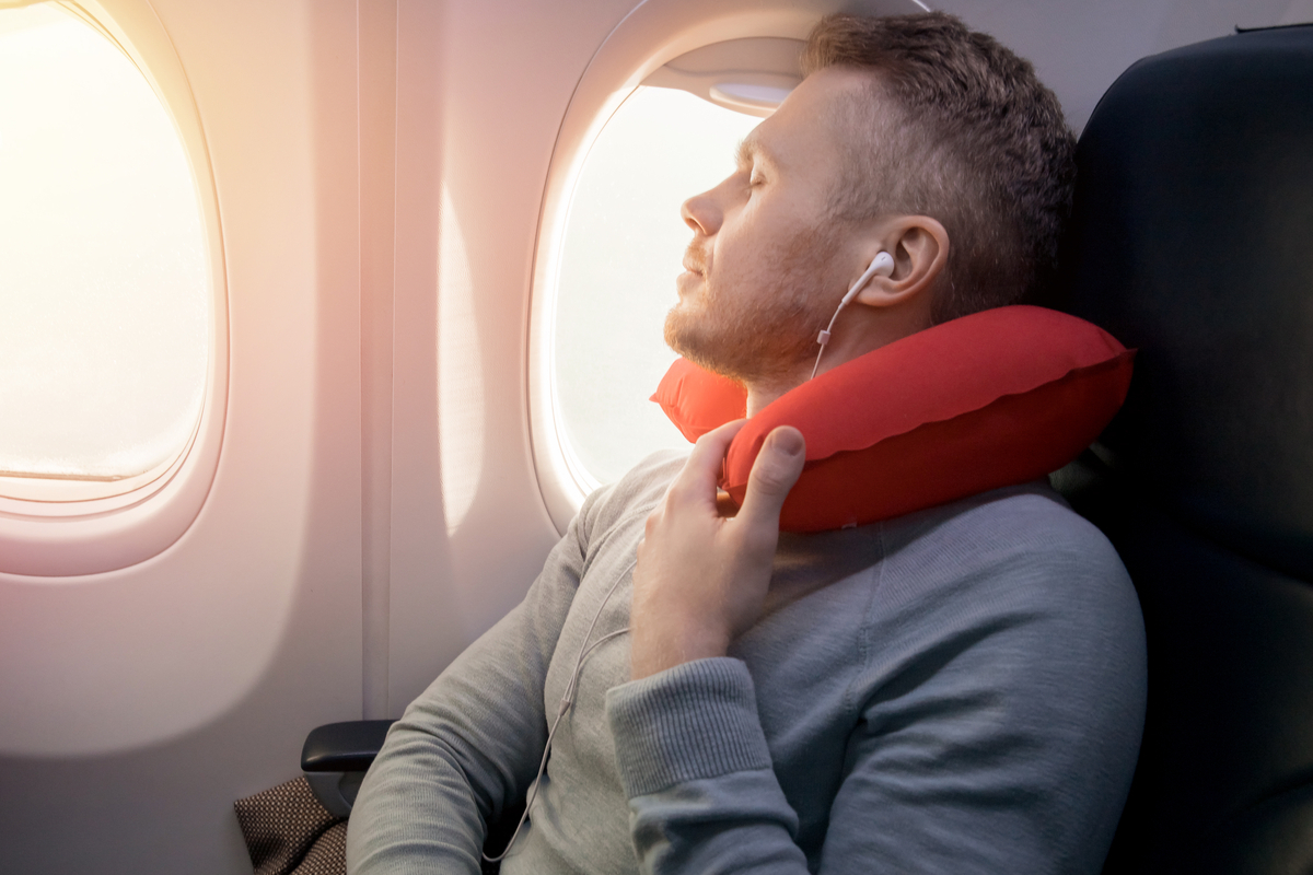 man sleeping on an airplane with neck pillow and headphones