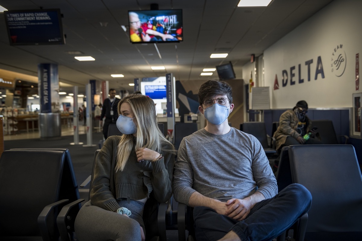 New York City, USA - March 21, 2020: A young man and woman wait at LaGuardia airport to board a flight to Orlando. On account of the ongoing coronavirus pandemic, they were among the many passengers wearing respirator masks for protection.