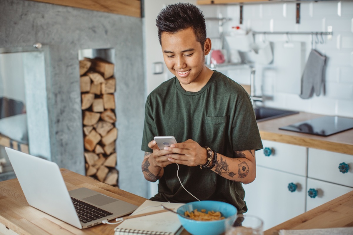 young man texting while studying on his laptop and eating cereal