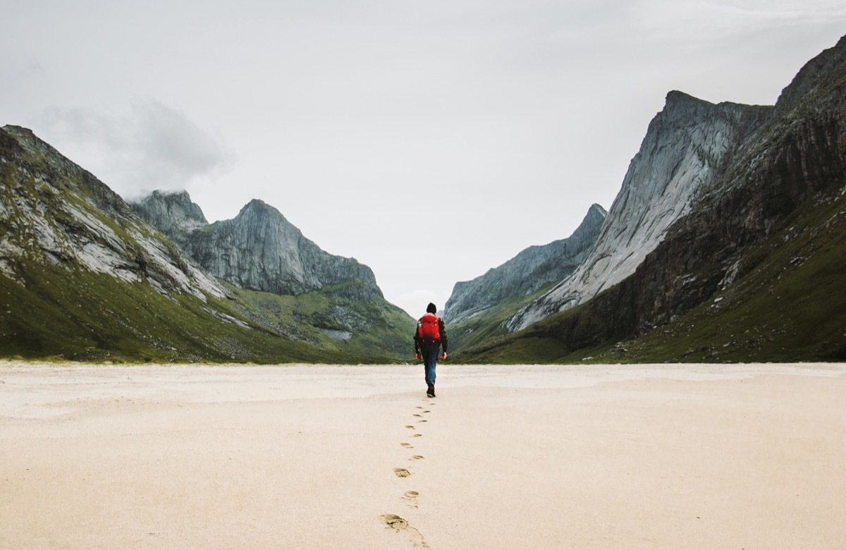 man with backpack walking alone at the beach