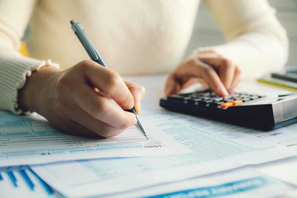 A person sitting and filling out their personal income tax forms while using a calculator