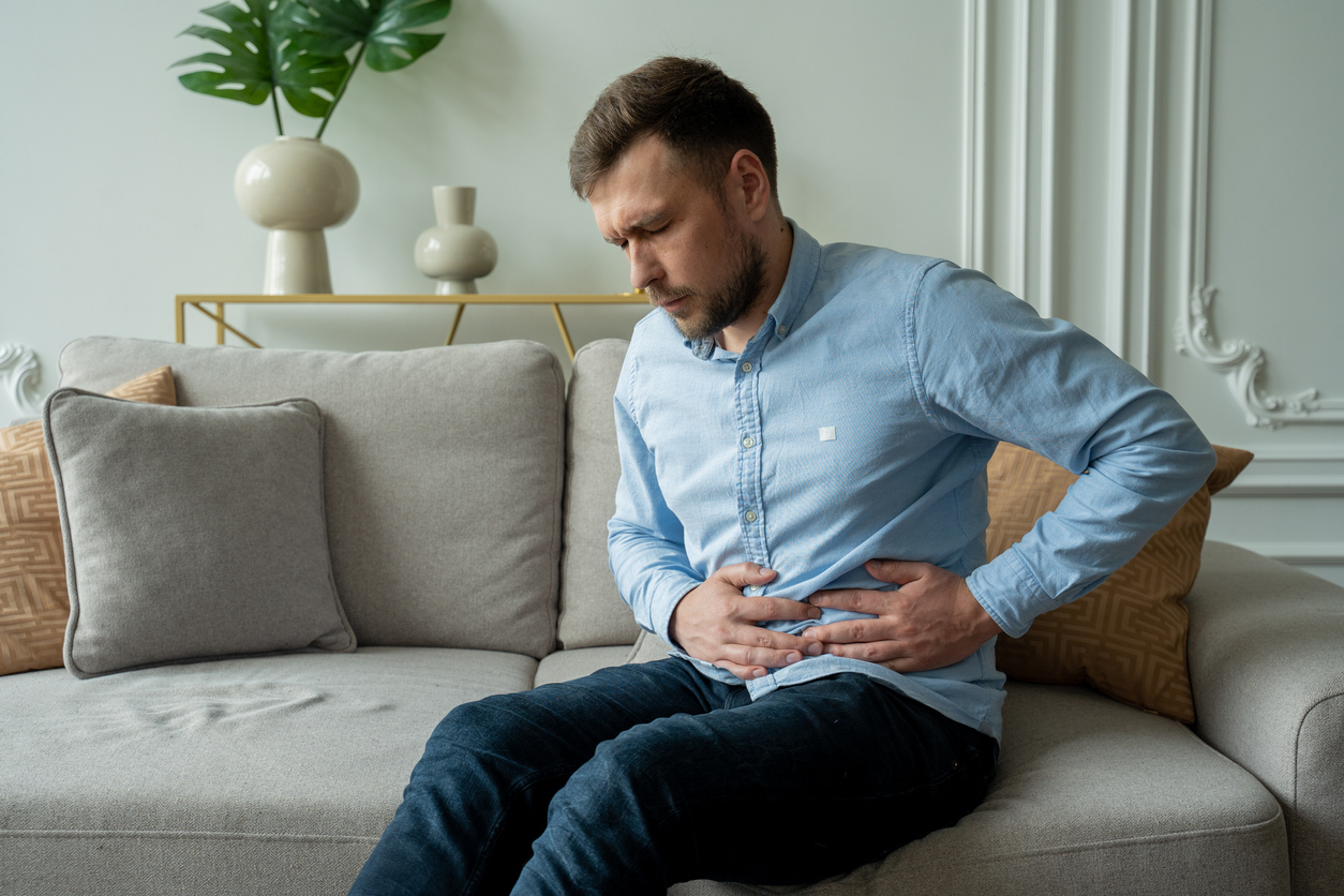 Man sitting on the couch clutching his side.