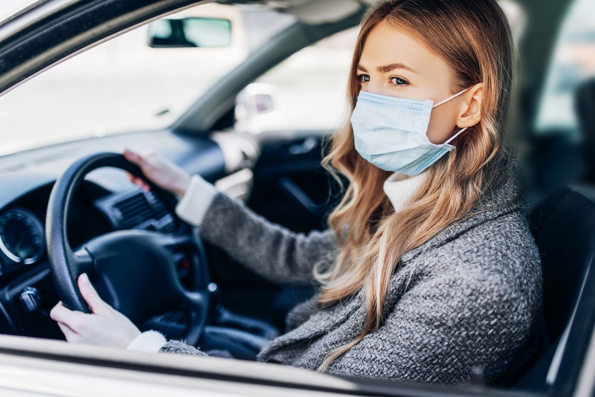 woman sitting inside a car, wearing a light blue mask