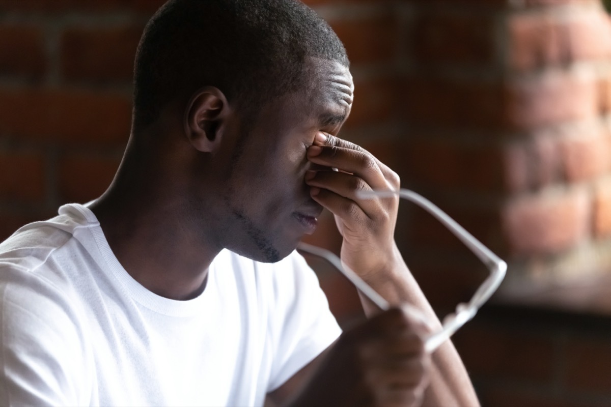 Close up black african man taking off glasses feels unhealthy suffering from eye strain after long working on computer