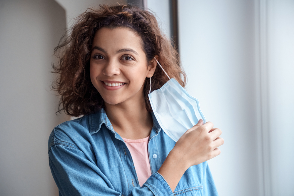 A young woman taking off her protective face mask and smiling