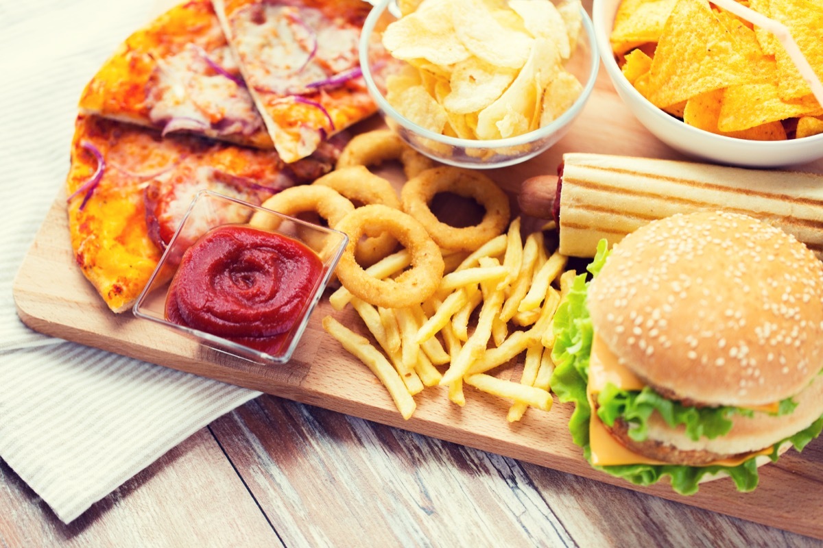 fast food and unhealthy eating concept - close up of hamburger or cheeseburger, deep-fried squid rings, french fries, pizza and ketchup on wooden table top view - Image