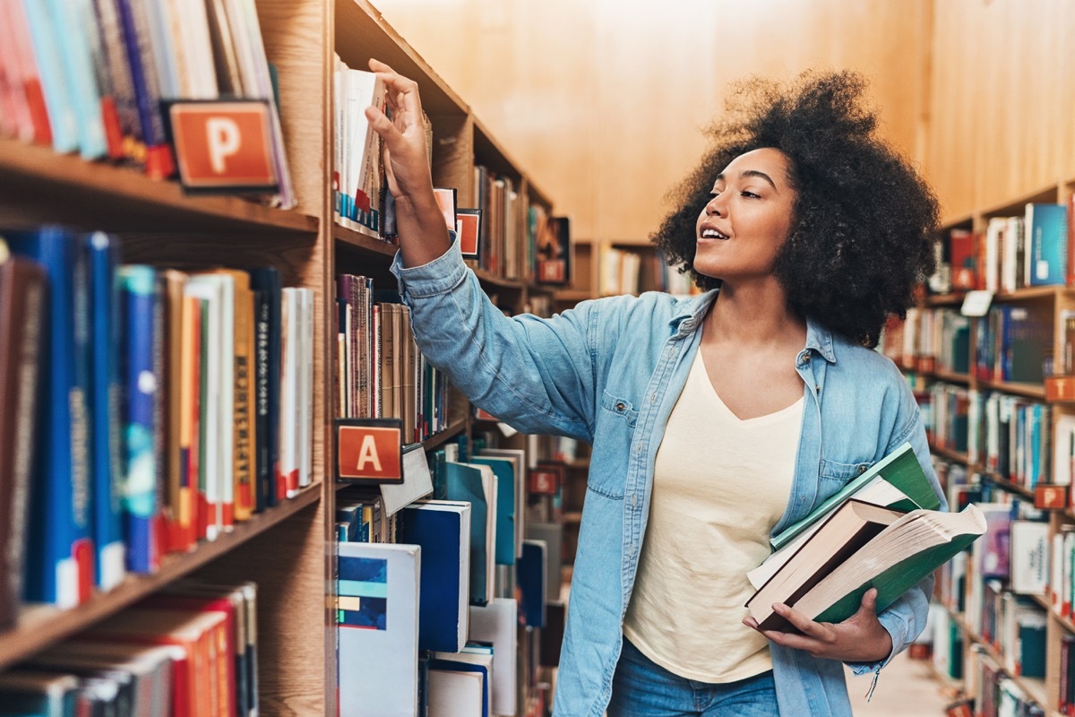 Student holding a stack of books in a library