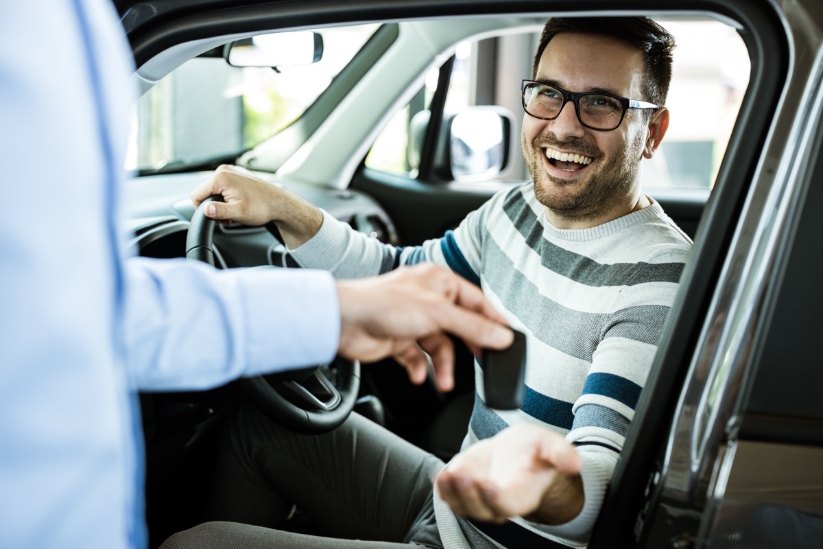 Happy man receiving keys for his new car in a showroom.