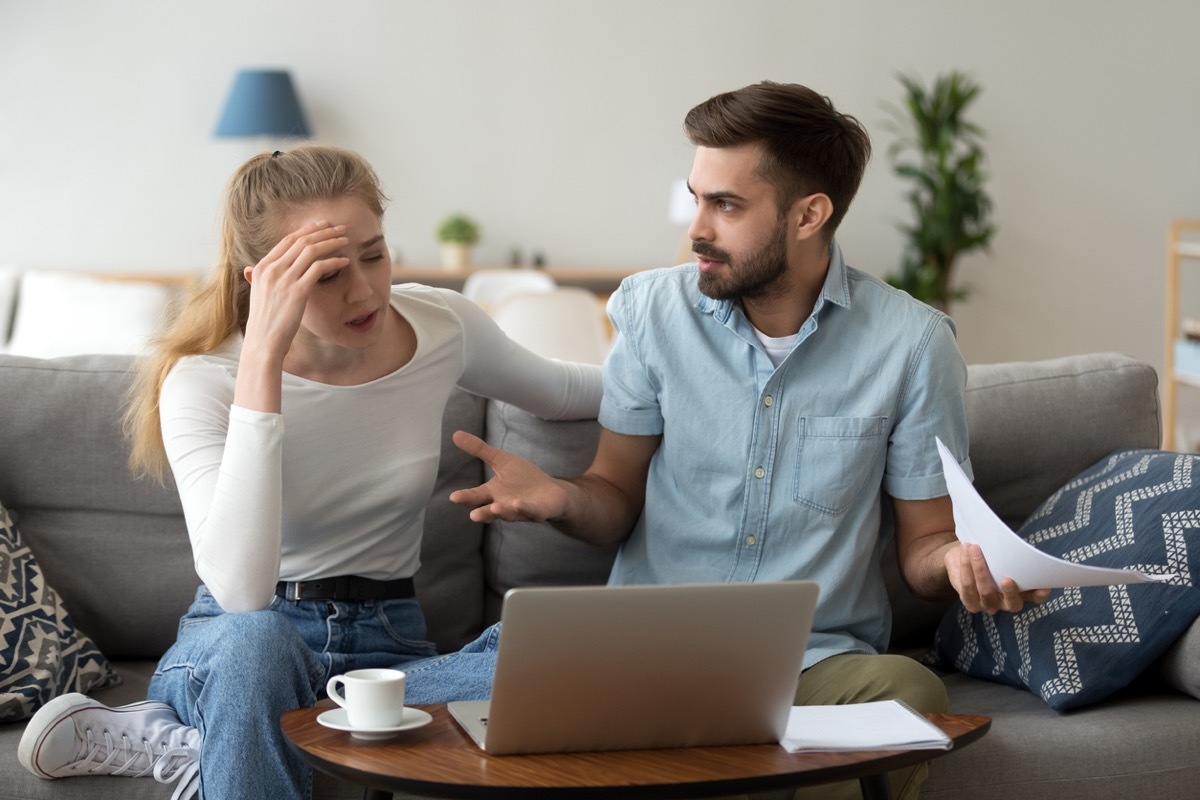 white woman with her hand on her forehead and white man putting his arms out while they hold papers and look at a laptop