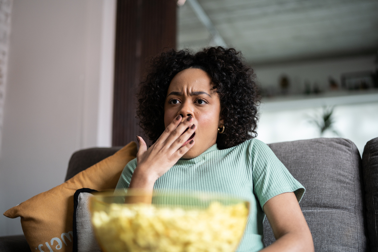 Young woman watching TV and eating popcorn at home