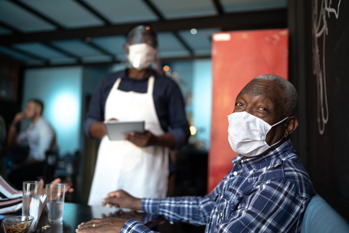 senior customer while waiter taking order at restaurant amid covid, both are wearing masks