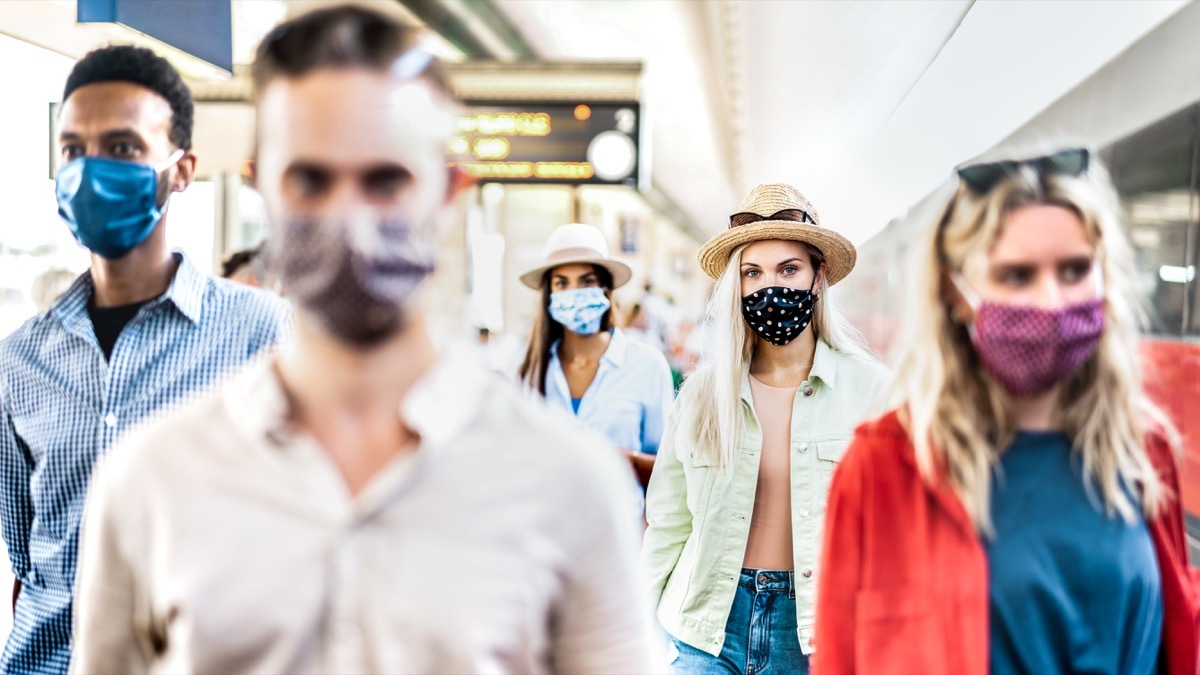 group walking with serious face expression at railway station - New normal travel concept with young people covered by protective mask - Focus on blond girl with hat