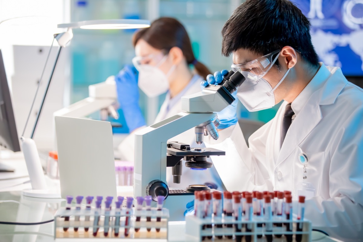 Asian microbiologist biotechnology researcher using microscope in the lab.