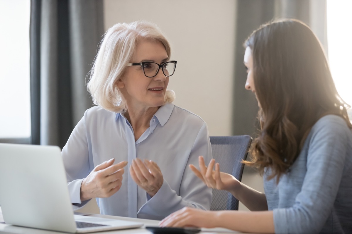 mature and young women colleagues sitting at desk talking about project startup ideas, sharing thoughts, solve currents issues, make research, discuss growth strategy, think how generate more revenue (Mature and young women colleagues sitting at desk