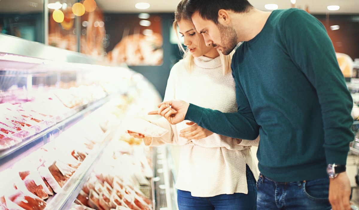 Closeup side view of a late 20's couple choosing some fresh meat for tonight's dinner. They are reading label on one of the packages and seem a bit uncertain about it.