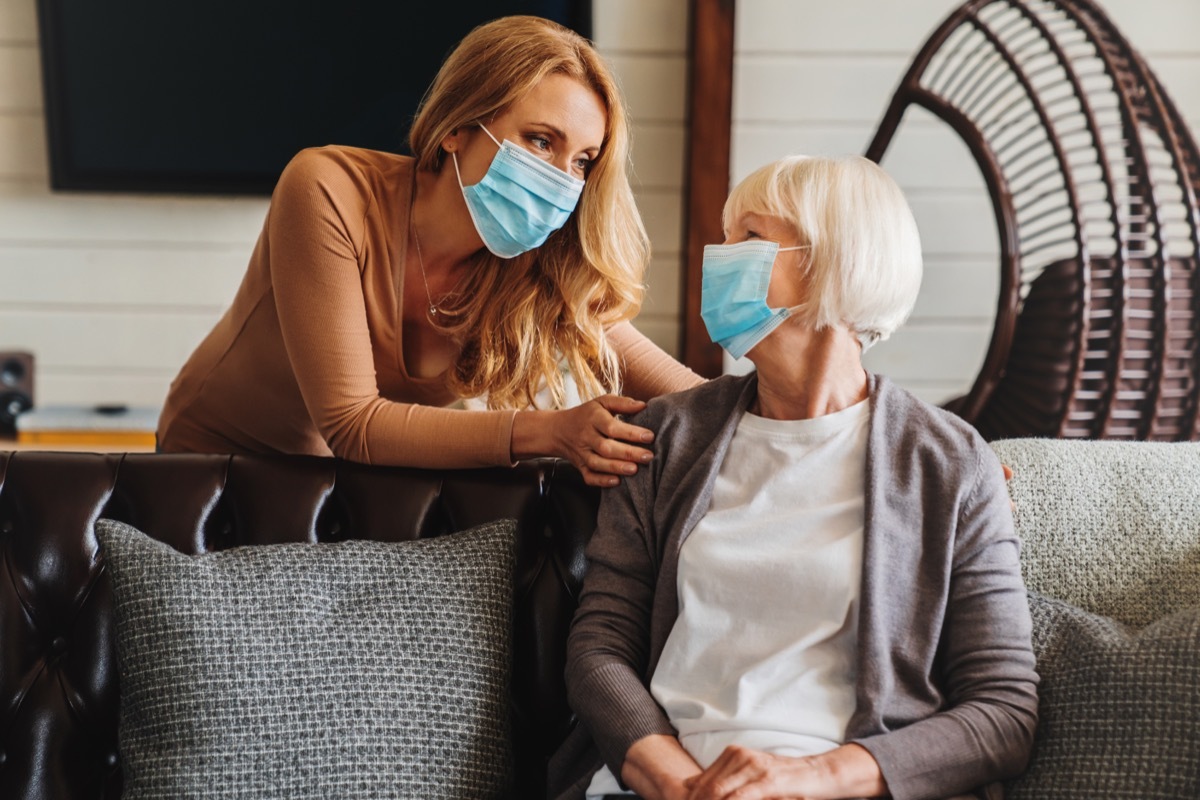 Senior woman in medical mask with young woman visiting her at home