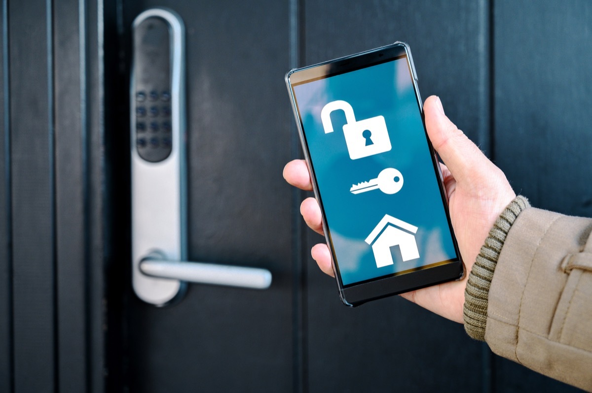 Concept of internet of things integrated in a smart home. Hand holds mobile phone with an app that controls the washing machine and tumble dryer. Could pass as both a home and also a laundromat.