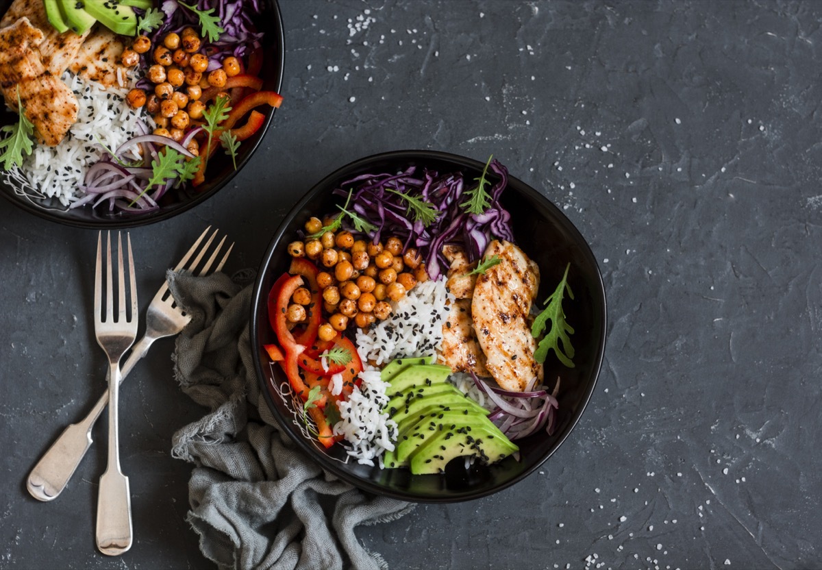 Grilled chicken, rice, spicy chickpeas, avocado, cabbage, pepper buddha bowl on dark background, top view. Delicious balanced food concept