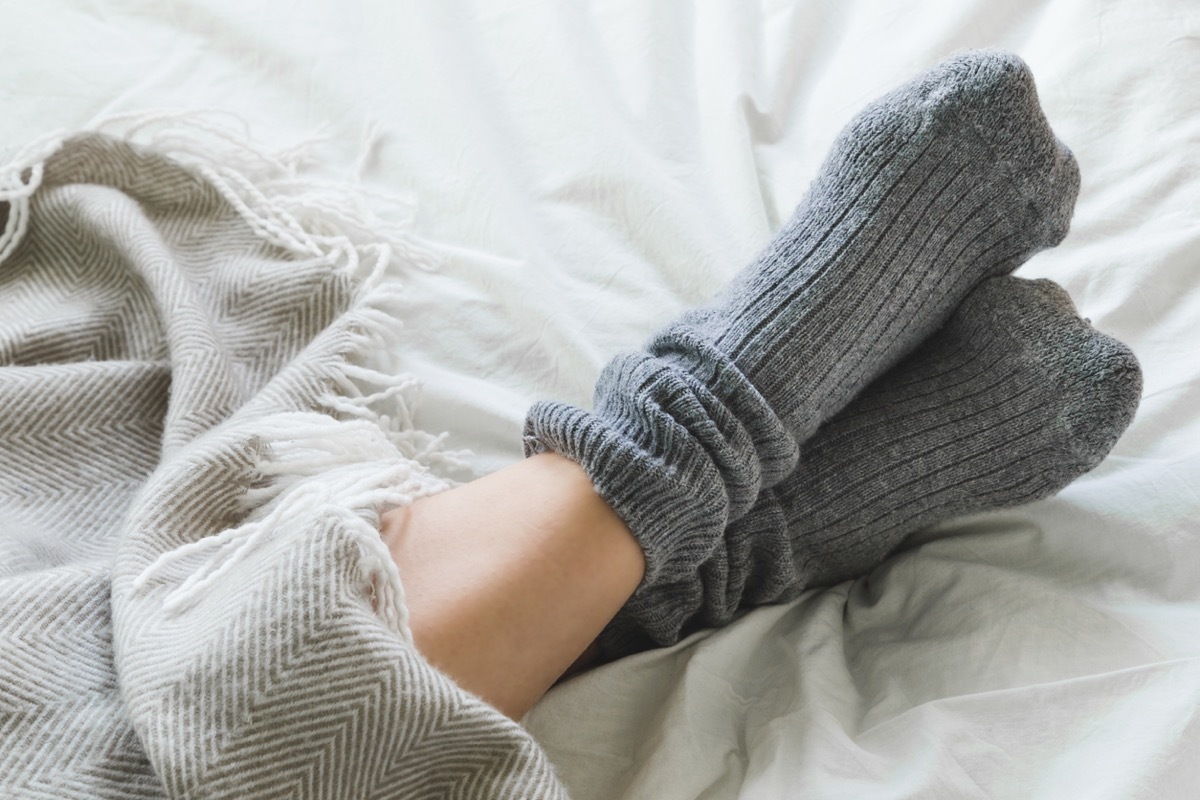 close up of crossed feet with socks on under a blanket in bed